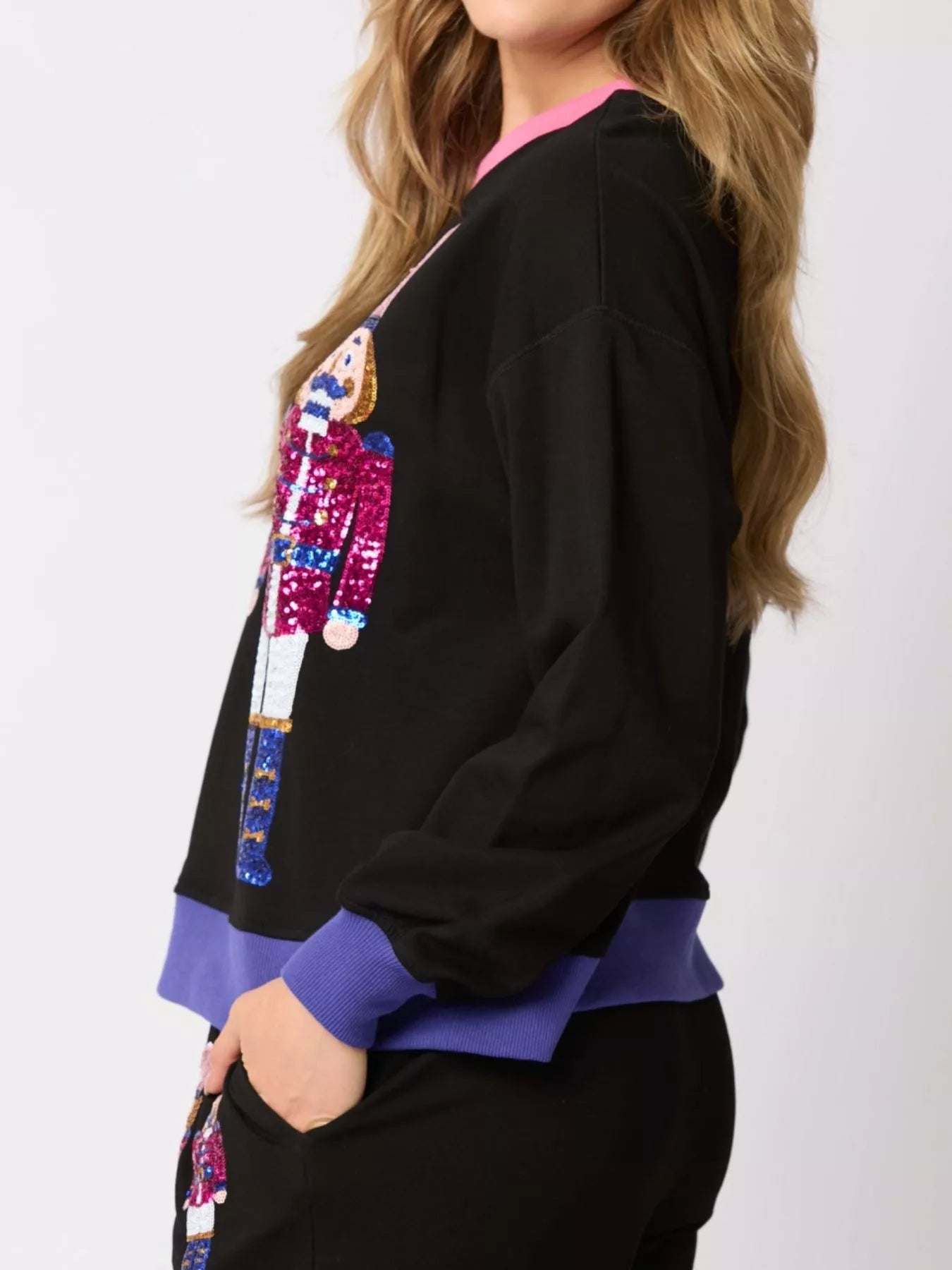 Person wearing a black sweatshirt with colorful sequin design on a white background